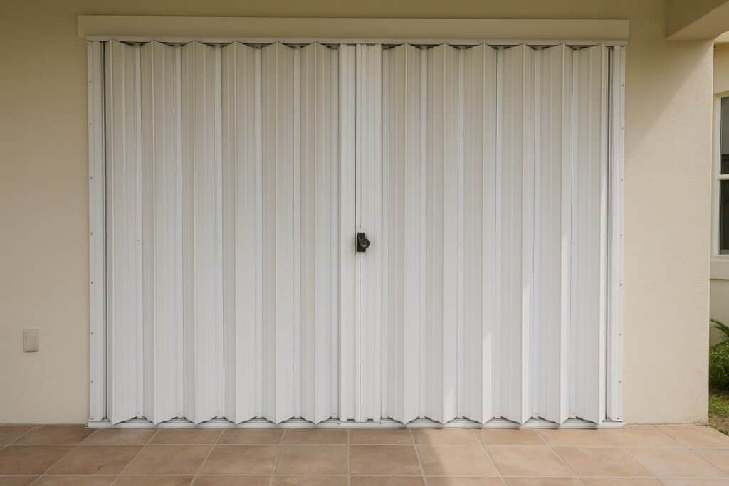 White accordion hurricane shutter closed across a sliding glass door