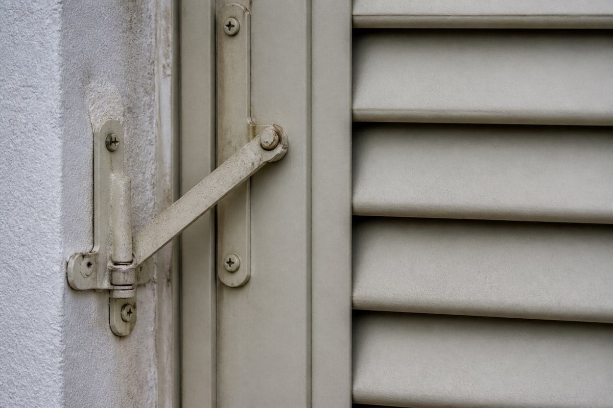 Close-up of a Bahama shutter hinge and prop-arm hardware in the closed storm position